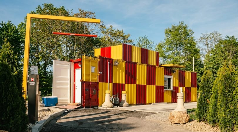 Drive-thru restaurant made from red and yellow shipping containers, surrounded by trees.