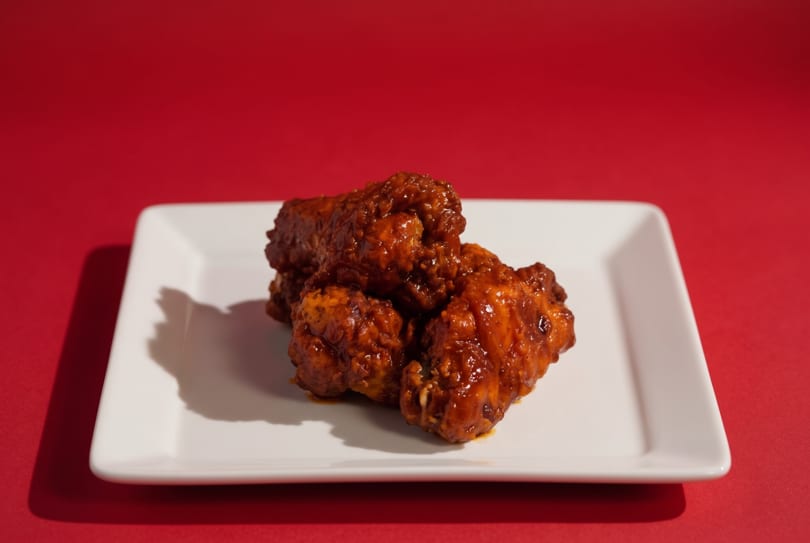 Four saucy buffalo chicken wings on a white rectangular plate against a red background.